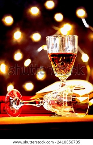 Stay home concept with a closeup picture of a glass of rose wine and a pile of red books with colorful bokeh lights