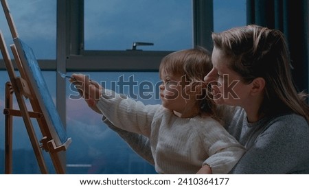 Mother teaching her little toddler how to draw a picture with oil paintings. Drawing together with momy, leisure activity with child at home.