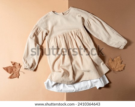 Top view flat lay beige children dress on beige and brown background. Royalty-Free Stock Photo #2410364643