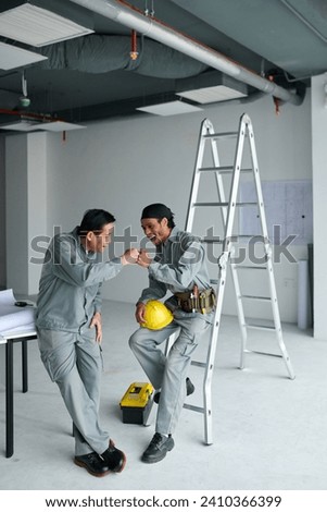 Workers making fist bump after finishing shift at construction site Royalty-Free Stock Photo #2410366399