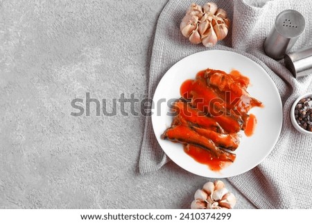 Composition with canned fish in tomato sauce, garlic and condiments on grey table