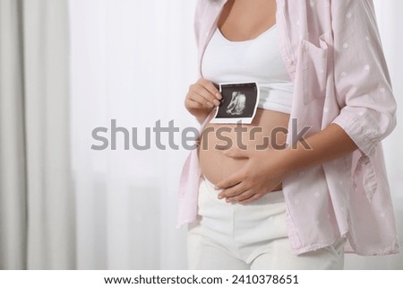 Pregnant woman with ultrasound picture of baby near window indoors, closeup. Space for text