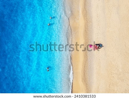Aerial view of blue sea, waves, sandy beach and umbrella with swimming people at sunset in summer. Tropical landscape with clear turquoise water. Top view from drone. Lefkada island, Greece. Travel