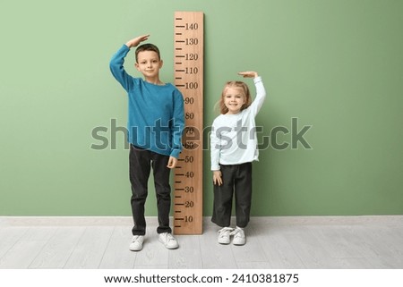 Cute little children measuring height near green wall Royalty-Free Stock Photo #2410381875