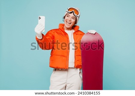 Young woman wear warm padded windbreaker jacket ski goggles mask hold snowboard do selfie shot mobile cell phone travel rest spend weekend winter season in mountains isolated on plain blue background
