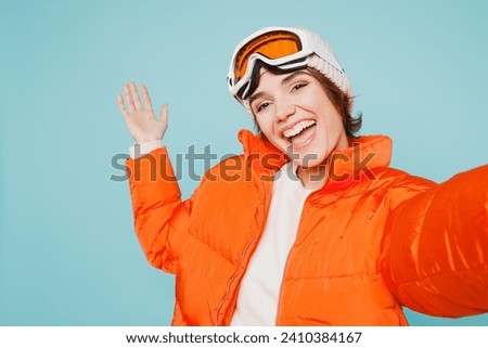 Close up skier young woman wear warm padded jacket hat ski goggles mask do selfie shot mobile cell phone travel rest going to spend weekend winter season in mountains isolated on plain blue background