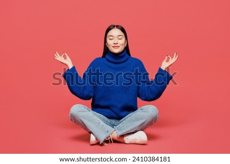 Full body young woman of Asian ethnicity wear blue sweater casual clothes sitting hold spreading hands in yoga om aum gesture relax meditate try to calm down isolated on plain pastel pink background