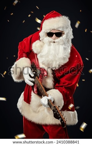 Party for Christmas and New Year. Modern Santa Claus in black sunglasses plays an electric guitar. Black background with confetti. Royalty-Free Stock Photo #2410388841