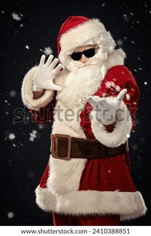 Celebrating Christmas and New Year. Modern Santa Claus in black sunglasses invites you to a party. Black background with snowfall. Royalty-Free Stock Photo #2410388851