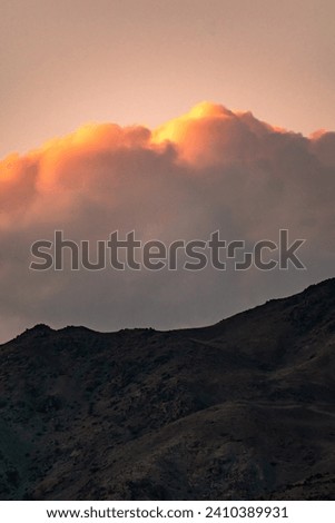A dramatic photo of the mountains of Tehran, Iran, with a cloudy sky and a play of shadow and light on the mountains