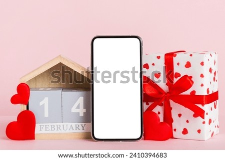 mobile phone with blank screen on colored background with hearts, calendar and gift box, valentine day 14 february concept perspertive view flat lay. Royalty-Free Stock Photo #2410394683