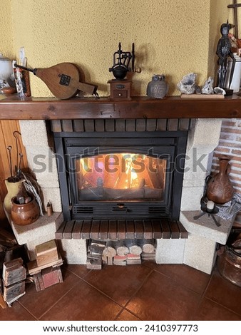 iron fireplace lit with wood fire. decoration of living room with bellows figures, coffee grinder, logs, pot and a candle