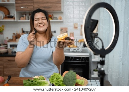 Asian Pregnant blogger looking at smartphone camera, she is live streaming cooking class for pregnant. Asian woman standing happily smiling at the kitchen counter preparing fresh organic salad. Royalty-Free Stock Photo #2410409207