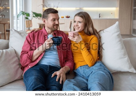 Loving couple man woman drink tea or coffee on cozy sofa at home, enjoy talking spending lazy weekend. Affectionate spouses wife husband bonding have comfort pastime. Harmonious marriage relationship. Royalty-Free Stock Photo #2410413059