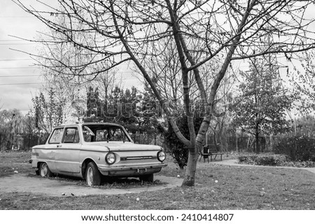 Photography on theme super old retro car Zaporozhets stands in park with flat tires, photo consisting of very old retro car with broken glass after an accident to park, old retro car at park no people