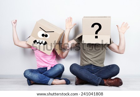 Couple with cardboard boxes on their heads sitting on floor near wall