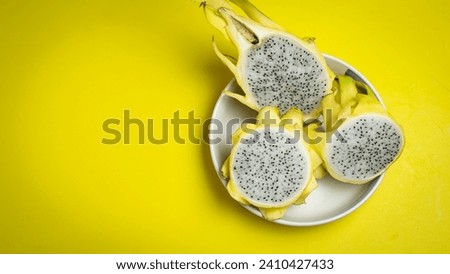 Top view, bright yellow dragon fruit cut in half, white flesh, sweet, juicy, delicious, healthy nutrition in a white bowl. on a yellow background
