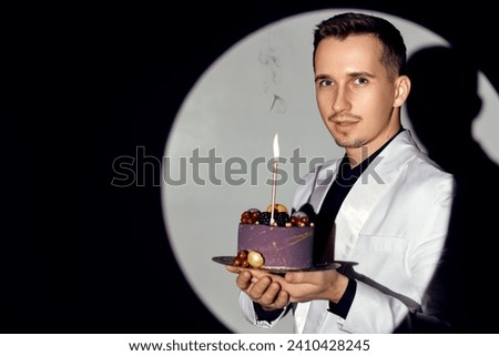 elegant caucasian man in white suit tuxedo holding cake with candle in the circle of light, copy space. Celebration