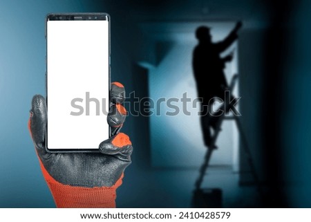 Phone in hand of electrician. Master is standing on stepladder. Smartphone with blank screen. Copy space in mobile phone. Place for electrician contacts. Handyman advertising template. Art focus
