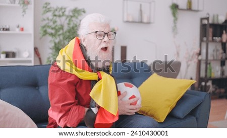 Close-up of a grandpa cheering for the German football team, watching the game at home as a devoted fan Royalty-Free Stock Photo #2410430001