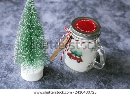 Christmas candles of white paraffin in a glass, decorated with a car and a Christmas tree on a gray background. High quality photo