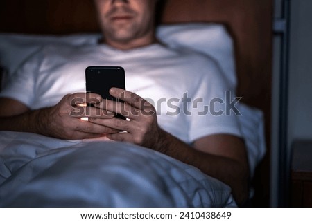 Phone in bed at night. Man with smartphone before sleeping. Secret texting, cheating or working late. Happy guy browsing online news. Holding cellphone in hand. Dark home bedroom. Screen time concept. Royalty-Free Stock Photo #2410438649