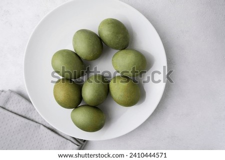 Green eggs in a white plate on a light background. Minimal concept. View from above. Easter eggs. Photos of preparations for Easter.