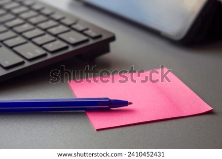 A blue pen lying on a pink sticky note beside a computer keyboard