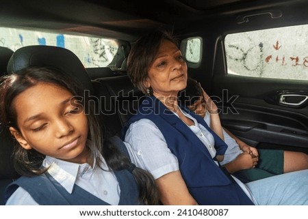An Indian pre-teen girl and her brother are fast asleep and leaning on their grandmother, after a long day at school in the back seat of their car in Mumbai, India.