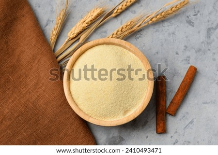 Bowl of raw semolina, cinnamon and spikelets on grunge background Royalty-Free Stock Photo #2410493471