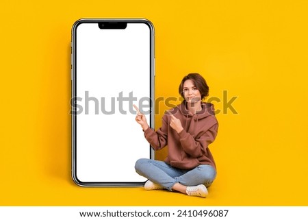 Full body size photo of young girl pointing finger empty space nomad phone touchscreen wear sweatshirt isolated on yellow color background