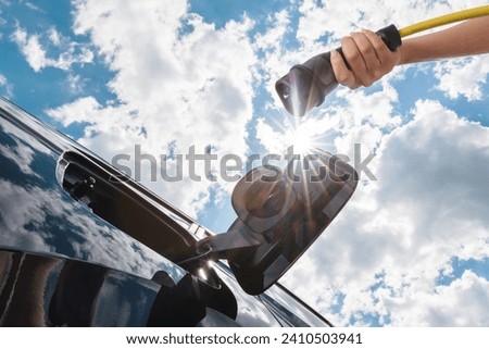 Female hand charging electric car with blue sky, photo from below