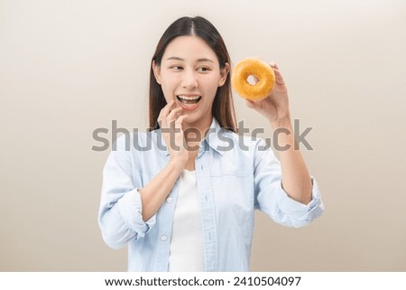 Portrait of pretty asian young woman holding dessert, donut glazed sugar, cute girl expression face enjoy sweet doughnut. Dieting for lose weight to slim. Eat fast food, snack junk food getting fat. Royalty-Free Stock Photo #2410504097