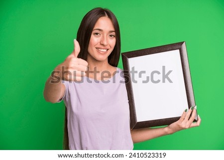 young pretty woman feeling proud,smiling positively with thumbs up with an empty blank picture frame