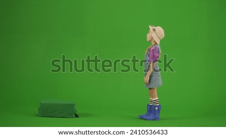 Portrait of girl in dress and rubber boots on chroma key green screen. Small cute girl gardener standing and looking up with amazed face.
