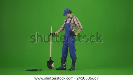 Portrait of farmer in working clothing on chroma key green screen. Gardener standing posing at camera with shovel in hand.