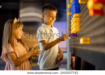 Kids making a picture with colored chips on the wall, playing on interactive models in science museum. Concept of children's entertainment and learning