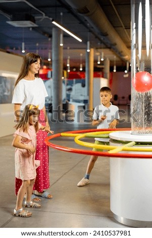 Mom with kids learn physics interactively on a model that shows physical phenomena while visiting a science museum. Concept of children's entertainment and learning Royalty-Free Stock Photo #2410537981