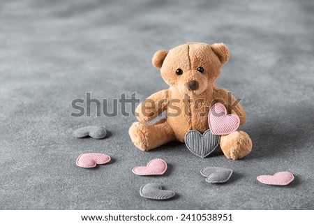 Teddy bear with hearts on a gray background. Valentine's Day. Side view, selective focus.