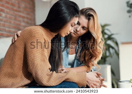 Shot of pretty young woman supporting and comforting her sad friend while sitting on the sofa at home. Royalty-Free Stock Photo #2410543923