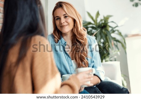 Shot of two smiling young women talking while drinking coffee sitting on couch in the living room at home. Royalty-Free Stock Photo #2410543929