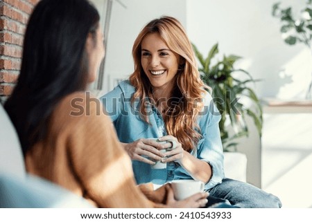 Shot of two smiling young women talking while drinking coffee sitting on couch in the living room at home. Royalty-Free Stock Photo #2410543933
