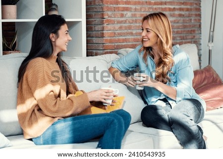 Shot of two smiling young women talking while drinking coffee sitting on couch in the living room at home. Royalty-Free Stock Photo #2410543935