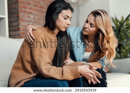 Shot of pretty young woman supporting and comforting her sad friend while sitting on the sofa at home. Royalty-Free Stock Photo #2410543939