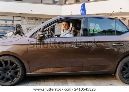 Young woman learning how to drive car together with her instructor. Driving school. Happy driving student. Brown car with blue L plate on a roof.