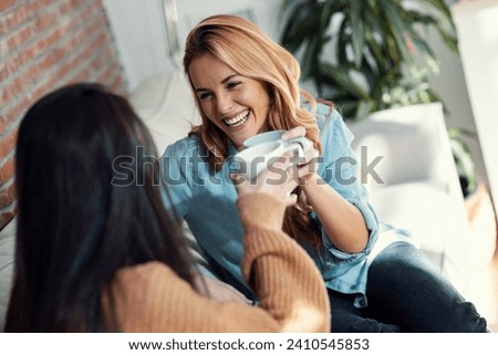 Shot of two beautiful female friends talking while toasting with a cup of coffee sitting on the couch at home Royalty-Free Stock Photo #2410545853