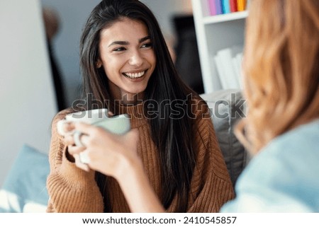 Shot of two beautiful female friends talking while toasting with a cup of coffee sitting on the couch at home Royalty-Free Stock Photo #2410545857