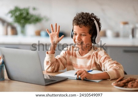 Black Little Boy Having Online Lesson, Making Video Call On Laptop At Home, Cheerful Preteen Male Child Wearing Wireless Headphones Waving Hand At Computer Webcamera, Enjoying Remote Education Royalty-Free Stock Photo #2410549097