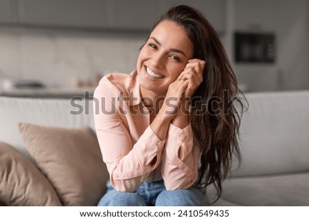 Radiant woman with contagious smile poses playfully, hands gently cradling her face, capturing moment of genuine happiness and effortless charm Royalty-Free Stock Photo #2410549435