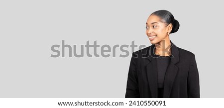 Side of a poised glad millennial African American businesswoman with a beaming smile, looking to the side, dressed in a sleek black blazer on a light gray background, panorama Royalty-Free Stock Photo #2410550091